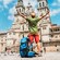 A man with a walking stick and backpack raising his hands in triumph in front of the Gothic cathedral of Santiago de Compostela